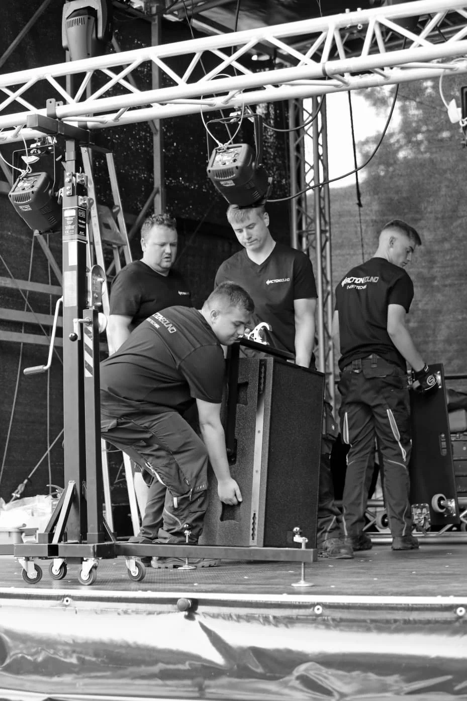 Das ActionSound-Team hebt Lautsprecherboxen und montiert Bühnenelemente bei einer Veranstaltung.