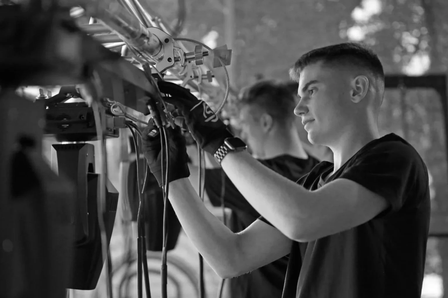 Ein Techniker von ActionSound schließt Kabel an eine Lichtanlage an einer Traverse an.