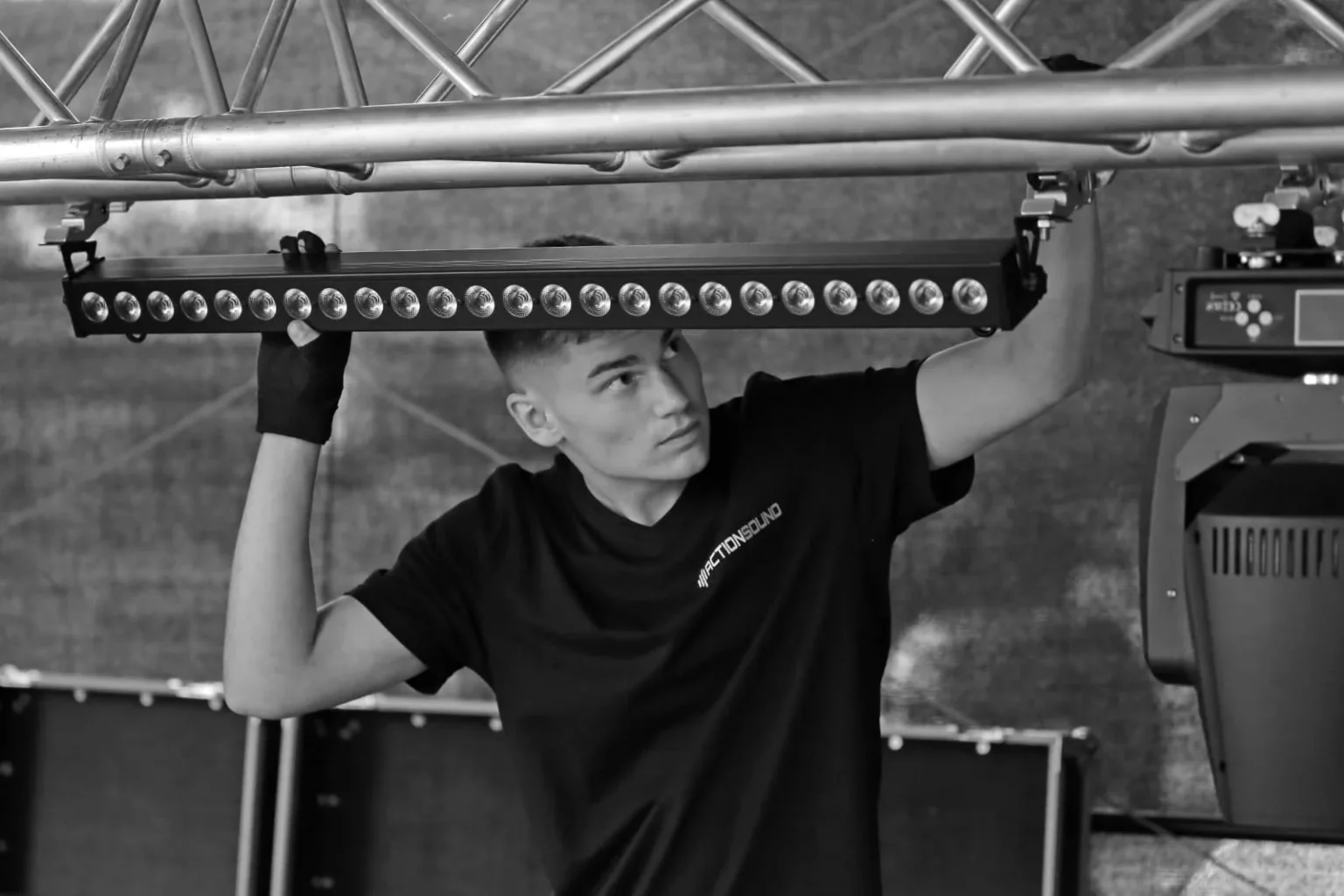 Ein ActionSound-Techniker montiert ein LED-Lichtsystem an einer Traverse für eine Veranstaltung.